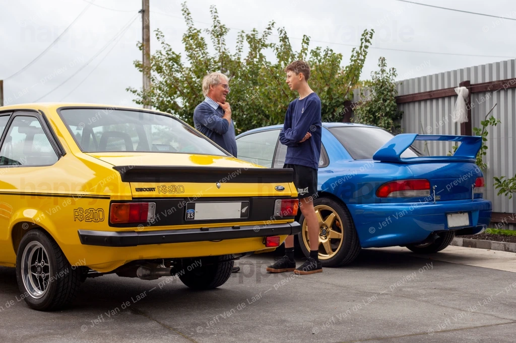 Two men talking between a yellow classic car and a blue sports car — Street photo by Jeff Van de Laar