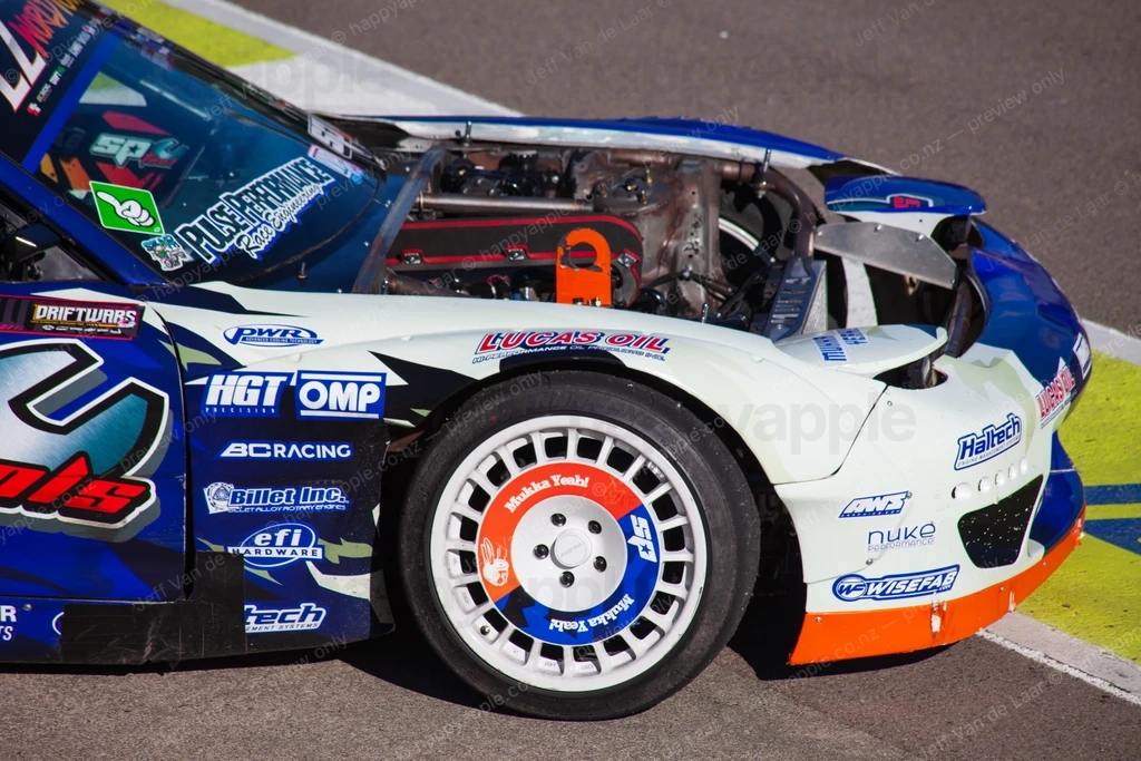 Race car with sponsor decals and exposed engine bay at a circuit — Automotive photo by Jeff Van de Laar