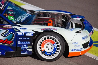 Race car with sponsor decals and exposed engine bay at a circuit